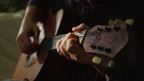 The guitarist plays a classic wooden guitar. A musician plays an acoustic guitar in a dark room. Close-up.