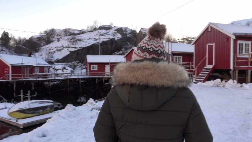 Young woman walking through the snowy red wooden cabin of the village of Norway
