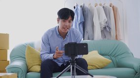 Businessman sitting in sofa video live streaming sell shirt e commerce store or blogger live broadcasting selling shirt by smartphone and sharing on social media by at home