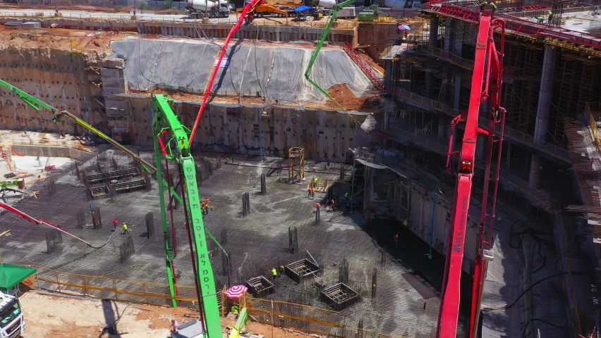 Tel Aviv, Israel - December 21, 2020: Multiple Concrete Pumps operation in a large Construction site, with workers guiding and casting a new floor level, Aerial view. 