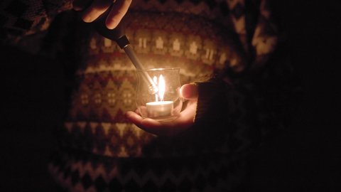 Person holding glass with tealight candle and Lighting with Lighter during dark night,close up shot. 