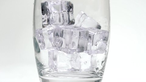 Soda or sparkling water pouring onto ice cubes filling up glass in slow motion bubbles close up carbonation white studio background