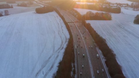 Drone footage of motorway surrounded by snow in fields with cars driving along the M25 in the morning for sunrise