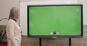 Mature woman using interactive screen with template green screen for communicating. Female professor talking and looking at digatal board in classroom. Concept of online learning