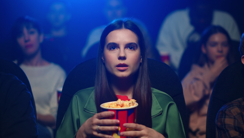 Portrait of young female person watching movie in dark hall. Attractive girl with long hair eating popcorn in movie theater in slow motion. Closeup beautiful woman enjoying interesting film in cinema. Royalty-Free Stock Footage #1066456414