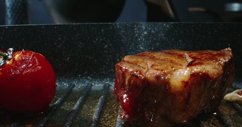 Close up shot of a juicy grilled steak on chef's preparation table. Smoke rising from big piece of tasty meat.
