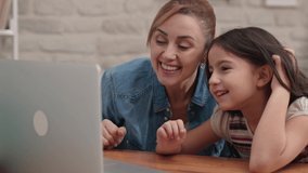 Girl and mother are video chatting at the working desk at the computer and shaking hands. Happy family. The concept of having a good time with their children.