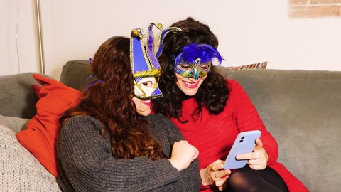 LGBT Lesbian couple girlfriends during pandemic carnival shooting selfie or having video-call wearing blue venice carnival mask. Concept quarantine, prevention COVID-19, Coronavirus situation