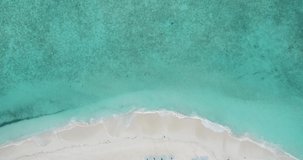 A drone rises over a beach in the Maldives, aerial view and waves wash ashore.