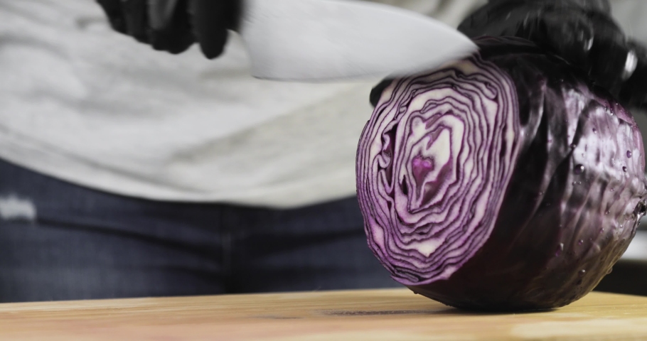 Cook is preparing vegeterian healthy food, salad. Woman chef is cooking cutting fresh red cabbage on wooden board, hands closeup. Slicing red cabbage in kitchen using knife.