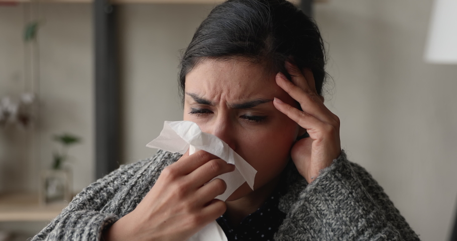 Close up head shot unhealthy millennial indian mixed race woman covered in warm plaid sneezing in paper tissue, having infectious disease, caught cold or suffering from grippe symptoms at home. Royalty-Free Stock Footage #1066471495