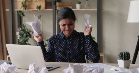 Stressed young mixed race indian business lady feeling nervous, doing paperwork. Anxious depressed female multiracial employee crumpling paper documents, standing leaving workplace, deadline concept.