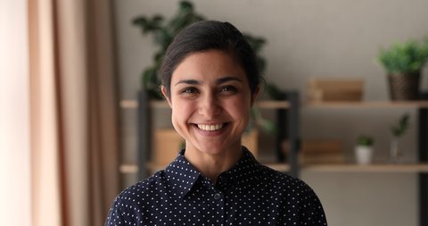 Head shot positive attractive millennial indian ethnicity business lady or company representative looking at camera, feeling confident indoors. Happy mixed race woman showing perfect wide smile.