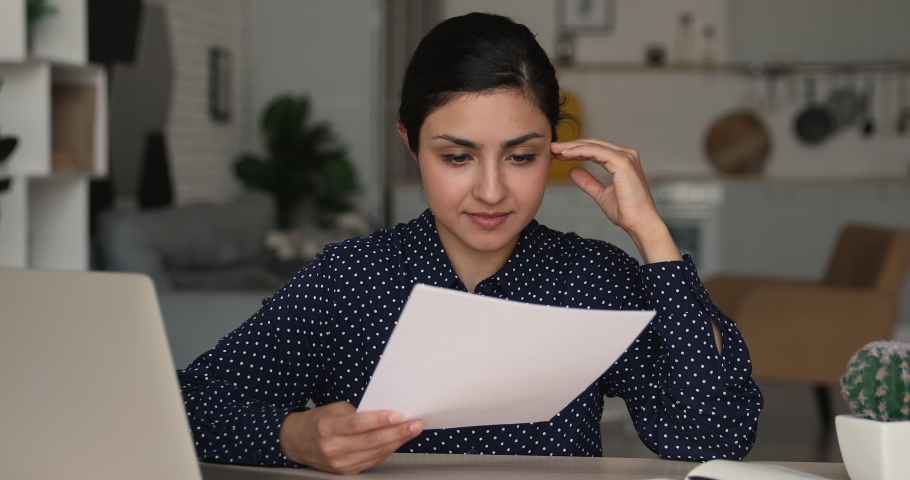 Focused young 25s indian ethnicity woman holding paper document in hands, feeling unhappy with exam failure, received negative news notification in correspondence, eviction notice or dismissal letter. Royalty-Free Stock Footage #1066471642