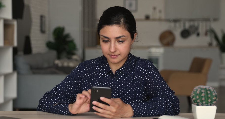 Stressed young multiracial indian woman typing using cellphone applications, feeling confused of bad electronic device work or getting message with unpleasant news, sitting at table at home office. Royalty-Free Stock Footage #1066471672
