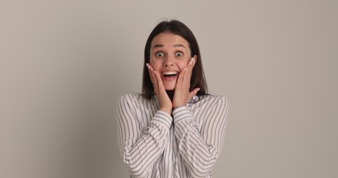 Happy young beautiful caucasian 25s woman looking at camera, hearing good unbelievable news, feeling surprised and amazed, showing sincere positive emotion omg reaction, posing near white wall.