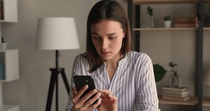 Happy attractive millennial woman using mobile phone, swiping photos in dating application, communicating distantly in social networks, checking email, reading news, playing games on cellphone indoors