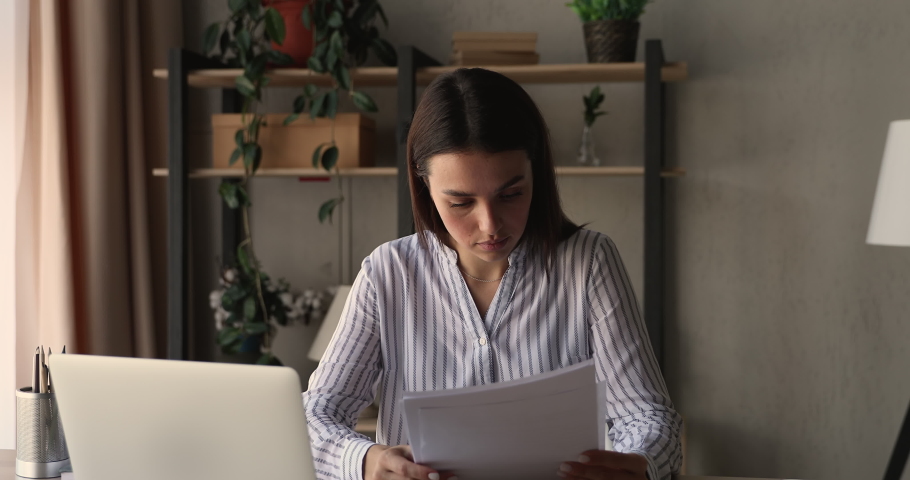 Concentrated young 25s businesswoman involved in financial paperwork, checking business reports, analyzing marketing sales marketing data statistics, working on computer alone at home or office. Royalty-Free Stock Footage #1066472437
