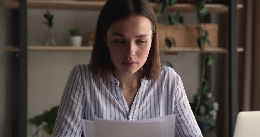 Frustrated young 25s woman reading paper letter with bad news, sitting at workplace Unhappy millennial businesswoman feeling confused with getting unpleasant information, thinking of problem solution. Royalty-Free Stock Footage #1066472506
