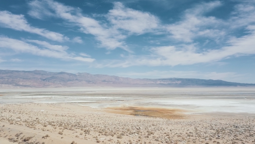 Straight forward aerial fly over colorful California salt flat terrain with beautiful cloudy blue sky and mountains. 