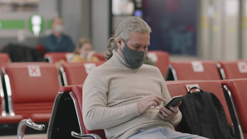 Medium shot of senior man in protective mask waiting for boarding in departure lounge in airport