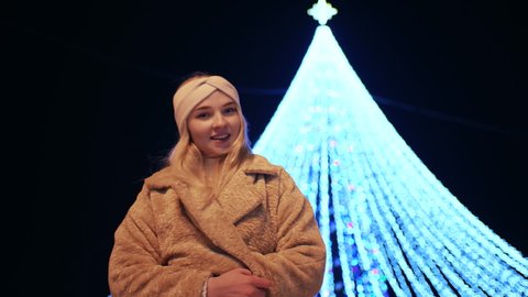 A girl poses against the background of a New Year tree in the evening in the city.