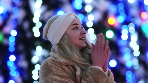 Beautiful girl freezes on the background of Christmas lights in the city.