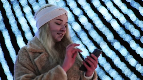 The girl against the background of Christmas lights of the evening city uses a smartphone.