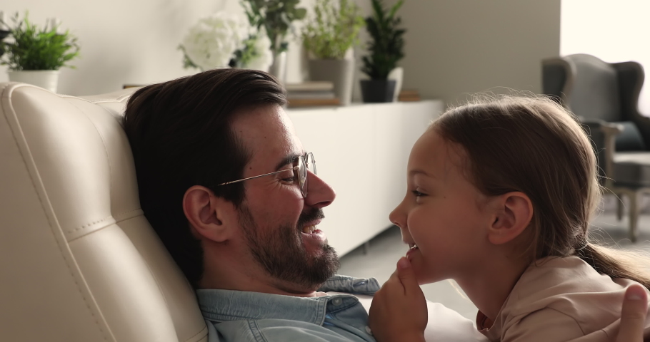 Loving 6s daughter spend weekend with caring daddy, people resting on armchair at home touch noses fooling enjoy priceless carefree time together, close up. Family bond, love, happy fatherhood concept Royalty-Free Stock Footage #1066486792