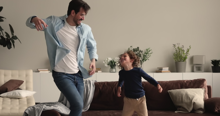 Preschool boy dancing with daddy at home. Active happy family listening favourite hit music moving jumping feel carefree spend weekend time together in modern warm living room. Leisure and fun concept Royalty-Free Stock Footage #1066486798