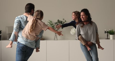 Family with preschool kids playing in living room, mom and dad carrying son and daughter running catching each other having fun enjoy active weekend at modern flat. Leisure activity at home concept