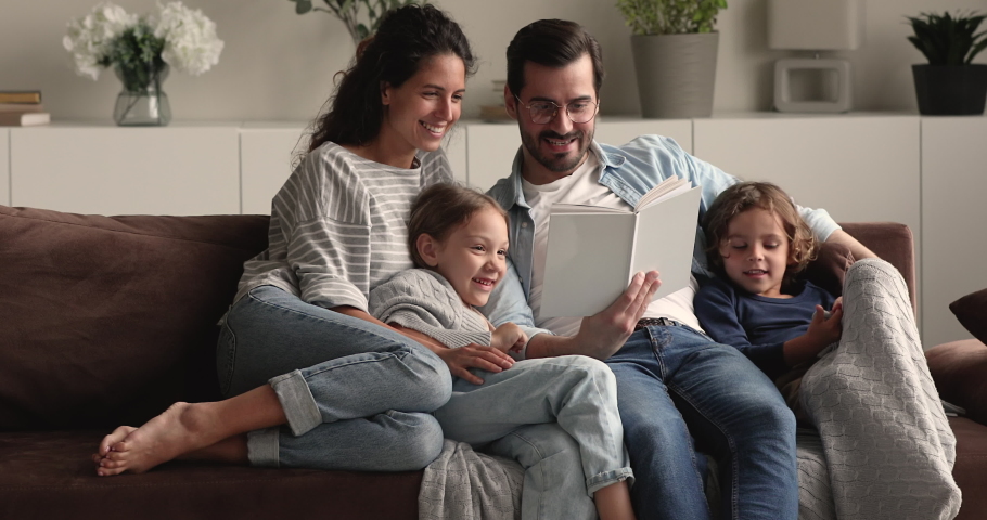 Full family gathered in cozy living room, couple and kids resting on comfy couch reading fairy tale to little curious attentive son and daughter. Development education of children, fun, hobby concept | Shutterstock HD Video #1066486948