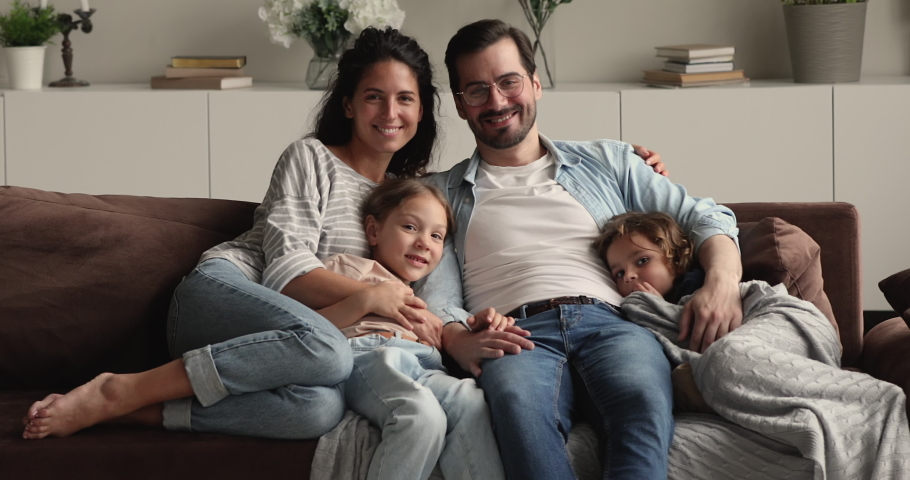 Portrait of happy lovely family with little kids sit on couch smile look at camera. Young parents rest on sofa hug preschool children spend weekend at modern home. Upbringing, happy parenthood concept Royalty-Free Stock Footage #1066486978