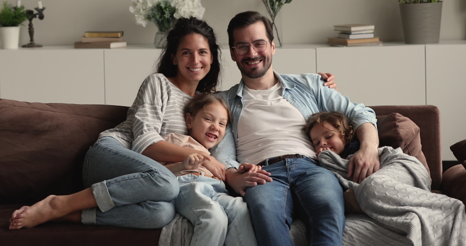 Portrait of happy lovely family with little kids sit on couch smile look at camera. Young parents rest on sofa hug preschool children spend weekend at modern home. Upbringing, happy parenthood concept | Shutterstock HD Video #1066486978