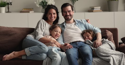 Portrait of happy lovely family with little kids sit on couch smile look at camera. Young parents rest on sofa hug preschool children spend weekend at modern home. Upbringing, happy parenthood concept