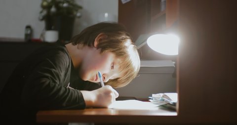 Homeschooling concept. A school-age child 8-9 years doing homework at home under the light of lamp.
