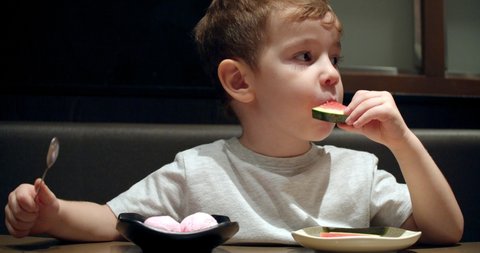 Cute healthy preschool kid boy eating ice cream with watermelon, banana fruit sitting in a children's cafe. Happy child eating healthy organic and vegan food in the restaurant. Childhood, health