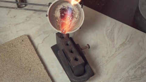 A jeweler pouring molten silver from a crucible into a mold.