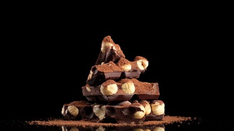 chocolate. stack of chocolate bar with nuts and cocoa powder on black background, rotating. dark chocolate with nuts. confectionery concept