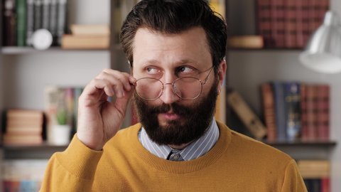 Skepticism, sarcasm emotion. Bearded man in glasses in office or apartment room looking at camera and expressing his skeptical attitude and discontent with his look. Close up and slow motion