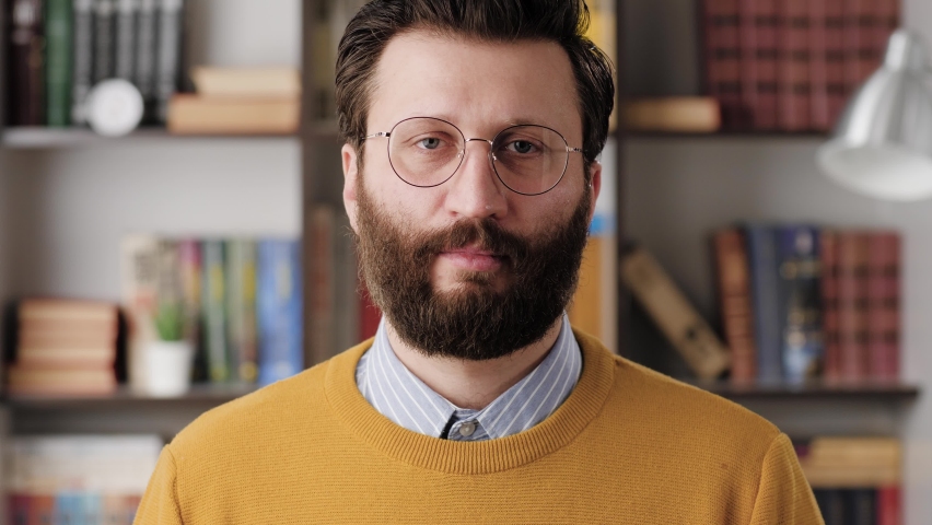 Shrug, i dont know. Perplexed bearded man in glasses in office or apartment room looking at camera and emotionally squeezes his shoulders and spreads his hands to show his ignorance. Close up Royalty-Free Stock Footage #1066509157