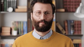 Shrug, i dont know. Perplexed bearded man in glasses in office or apartment room looking at camera and emotionally squeezes his shoulders and spreads his hands to show his ignorance. Close up