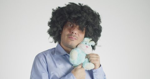 Front view of a curly-haired embracing and cuddling his plush bunny isolated on gray background.