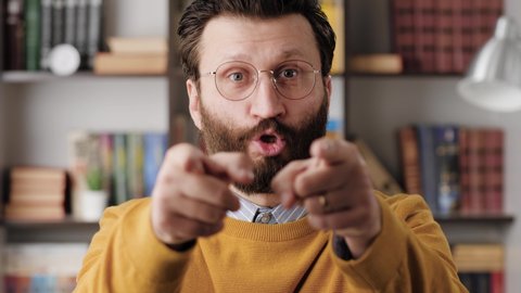 Man points his finger to you. Serious frowning bearded man with glasses in office or apartment room looking at camera and points his finger and says YOU. Close-up and slow motion