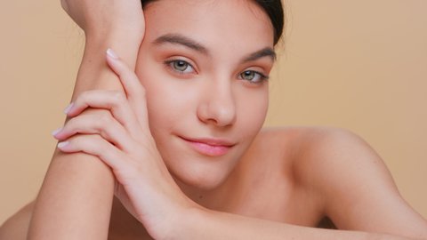 Close-up beauty portrait of young brunette woman with pure skin gently touches her face with hands sliding back of her hand from chin up along a jawline | Skin care products promotion concept