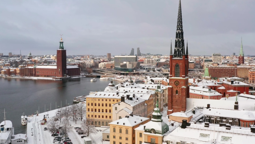 Stockholm island and buildings in winter. Swedish stadshuset and riddarholmen with white snow an anchoring boats and tall church. Colorful architecture facades in drone aerial view. Sweden  Royalty-Free Stock Footage #1066517443