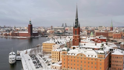 Stockholm island and buildings in winter. Swedish stadshuset and riddarholmen with white snow an anchoring boats and tall church. Colorful architecture facades in drone aerial view. Sweden 