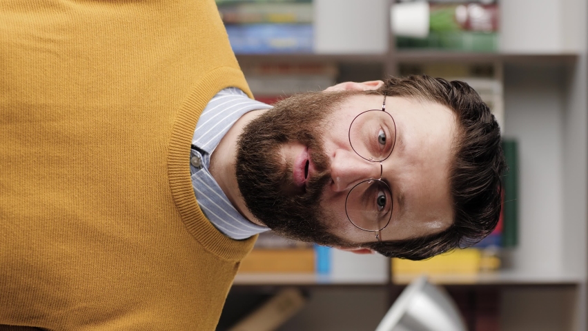 Shrug, i dont know. Vertical video of perplexed bearded man in glasses in office or apartment room looking at camera and emotionally squeezes his shoulders and spreads his hands to show his ignorance Royalty-Free Stock Footage #1066518946