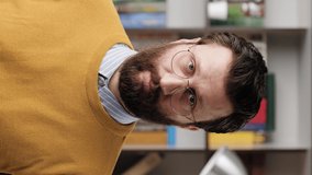 Man points his finger to you. Vertical video of serious frowning bearded man with glasses in office or apartment room looking at camera and points his finger and says YOU. Close-up and slow motion