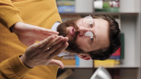 Man sarcastic applause. Vertical video of gloomy skeptical bearded man in glasses in office or apartment room looking at camera and reluctantly claps her palms to create fake applause. Close-up